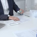 Business professional carefully examining financial documents. Using a magnifying glass and calculator. Auditing accounting reports. Analyzing tax data. Audit and taxes