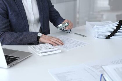 Business professional carefully examining financial documents. Using a magnifying glass and calculator. Auditing accounting reports. Analyzing tax data. Audit and taxes